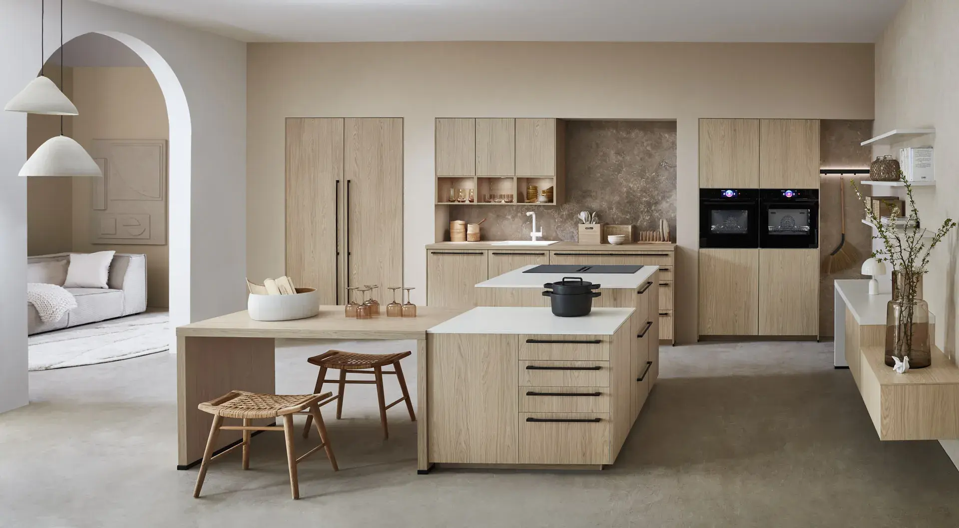 Hauptschuss, Mix aus Eichennachbildung und Premium Matt weiß, 2 Kücheninseln, eine mit Bosch Induktionskochfeld und Muldenlüfter, 2 Bosch Einbaubacköfen, Sitzbereich, 3 Oberschränke über der Spüle, Regalelement an der Wand, graue Nischenrückwand